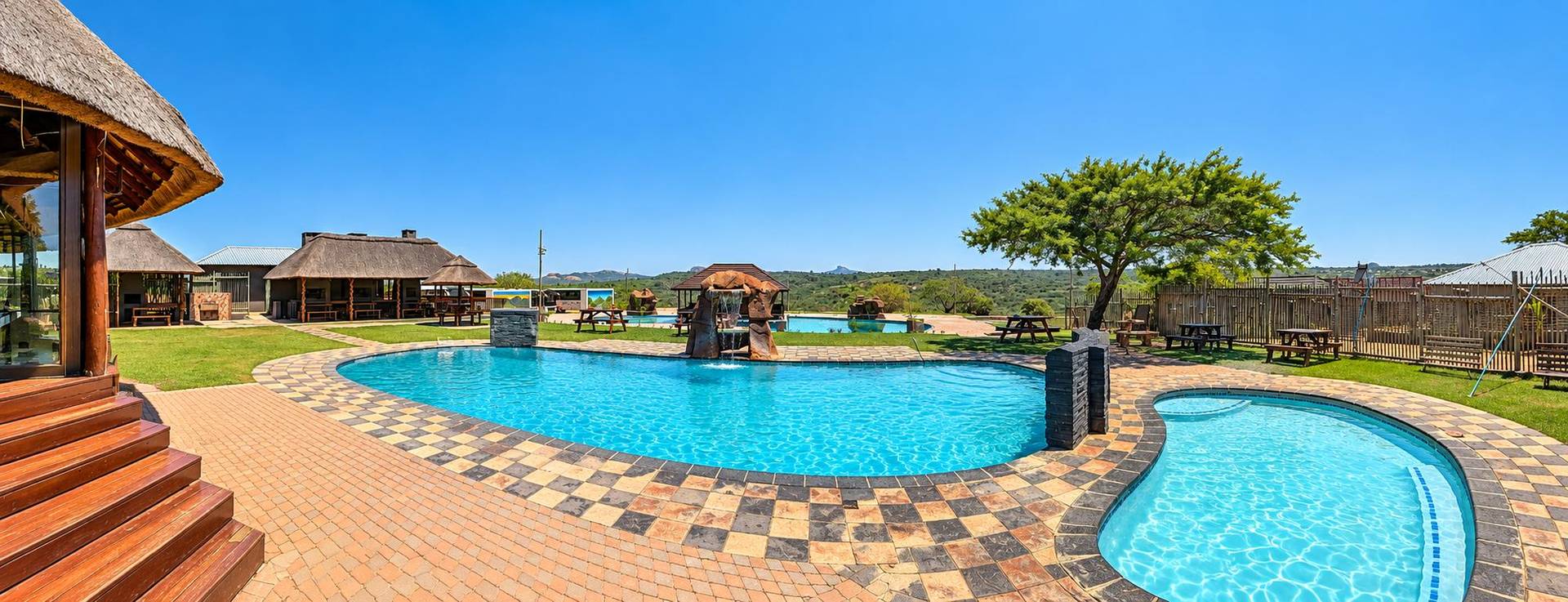 Numbigate Resort's pools and thatched lapas under a clear sky, with bushveld hills beyond