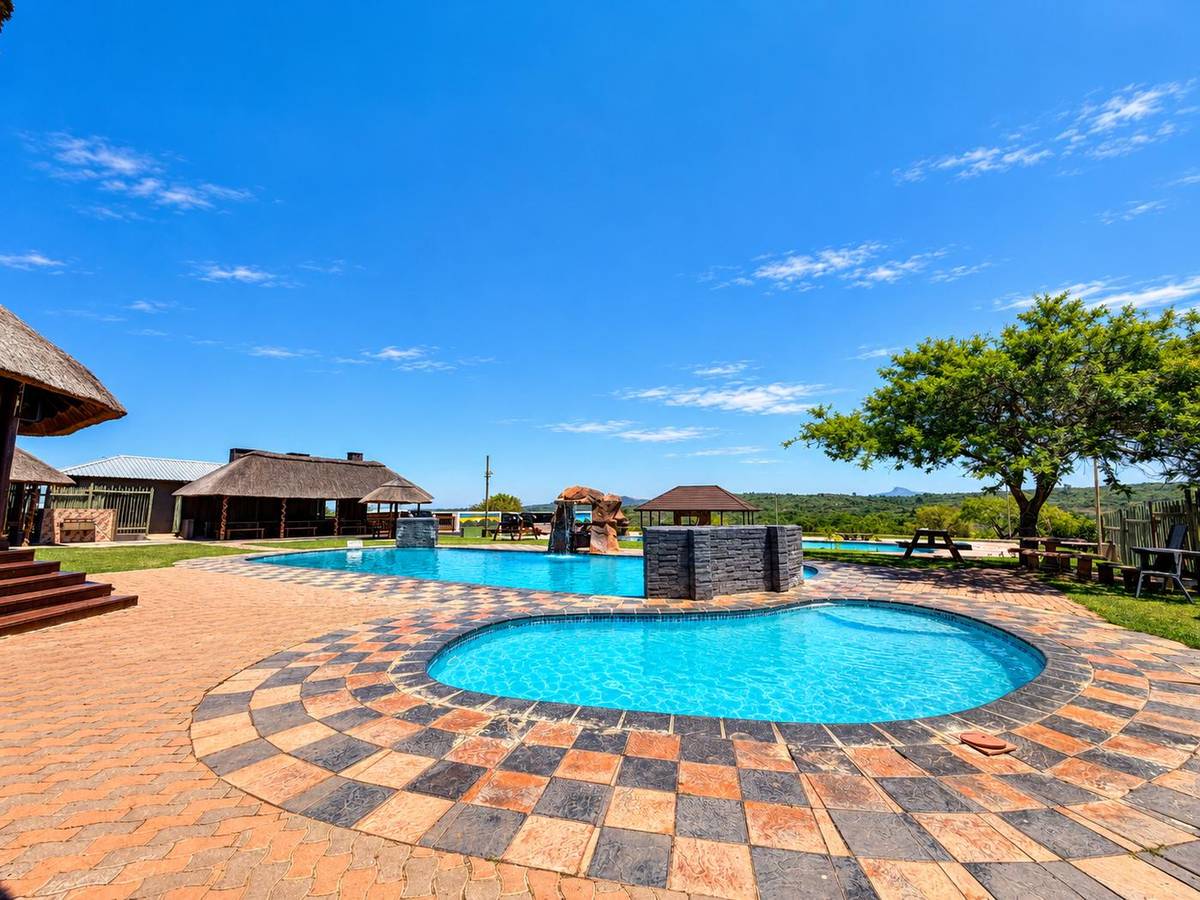 The kids' pool and main pool with rock waterfall, an acacia tree and hills behind
